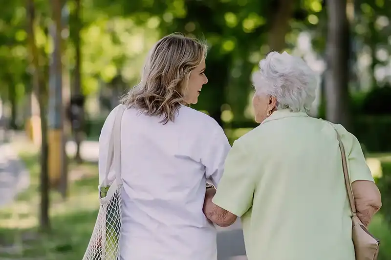 Jonge vrouw loopt buiten samen met oudere vrouw en houdt haar arm vast.