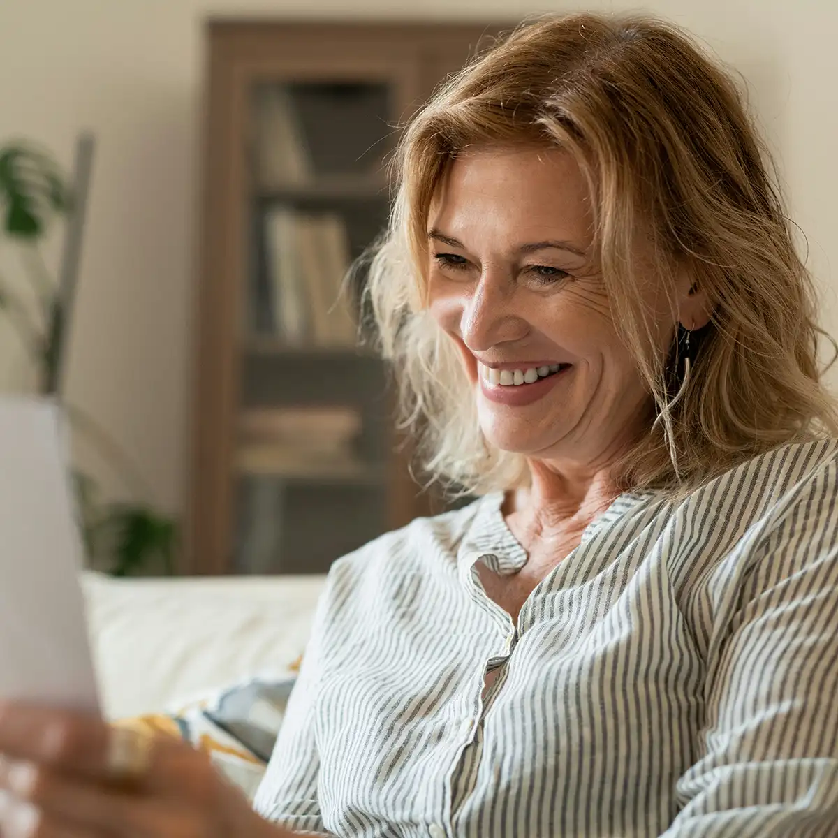 Vrouw die glimlacht terwijl ze een document leest in een comfortabele huiskamer.