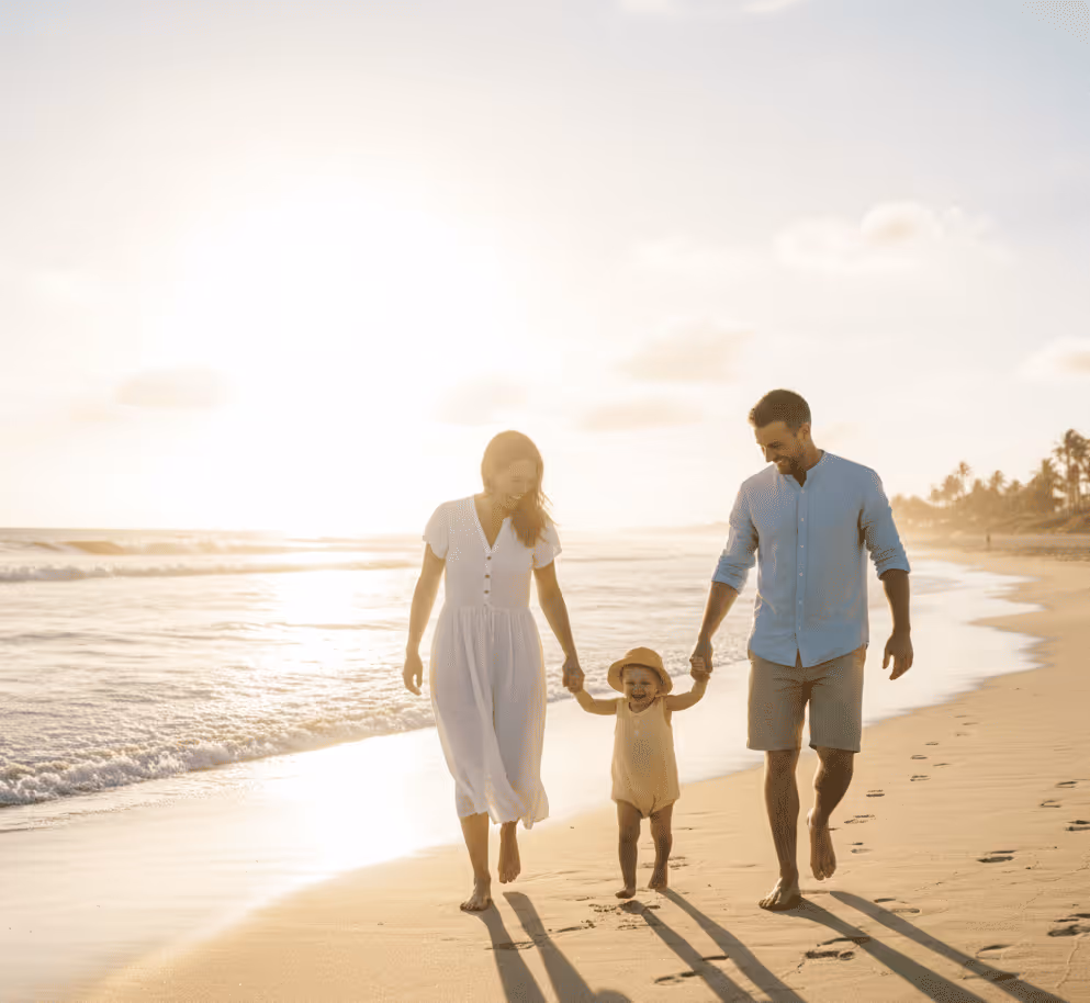 Familie mit Kind, die bei Sonnenuntergang barfuß am Strand spaziert und Hände hält.