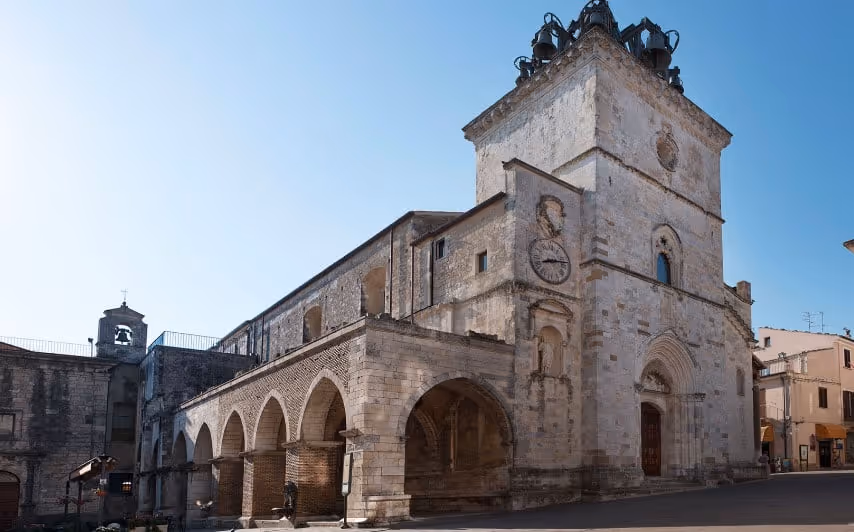 Stone historic church with arched colonnade and bell tower under clear blue sky.