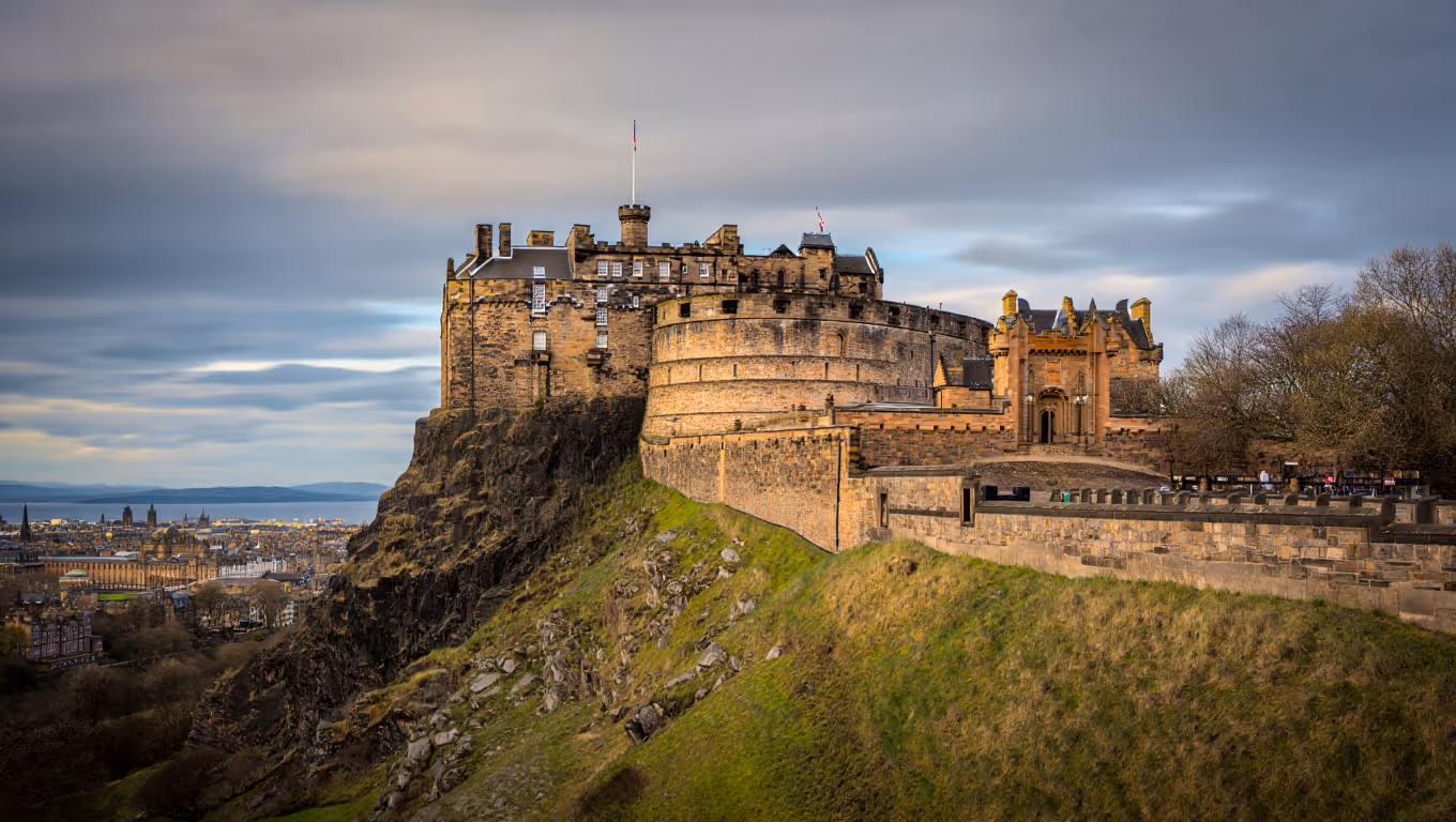 Edinburgh Castle perched on a rocky hill overlooking the city under a cloudy sky.