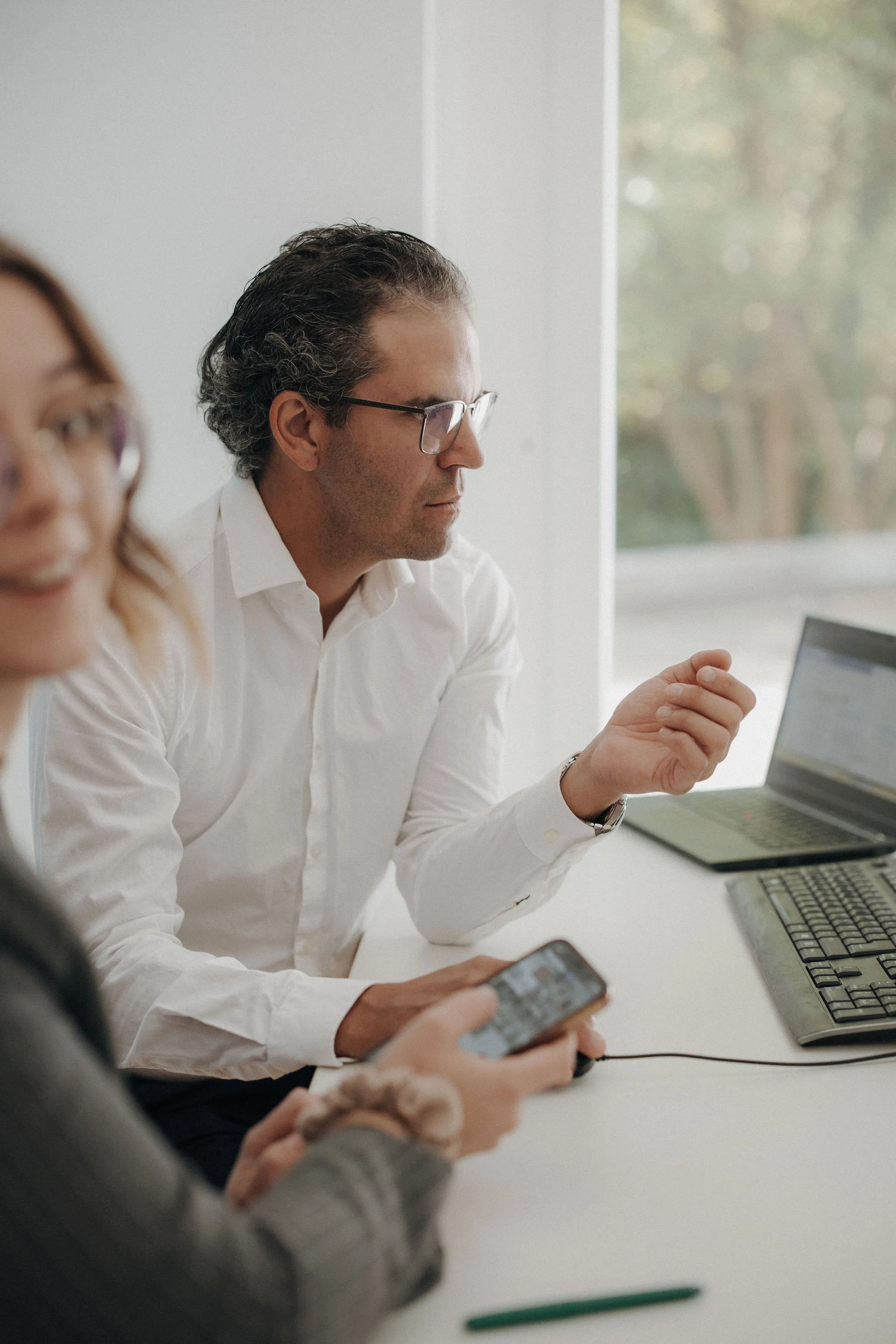 Zwei Personen sitzen an einem Tisch mit Laptop und Tastatur, eine Person hält ein Smartphone.