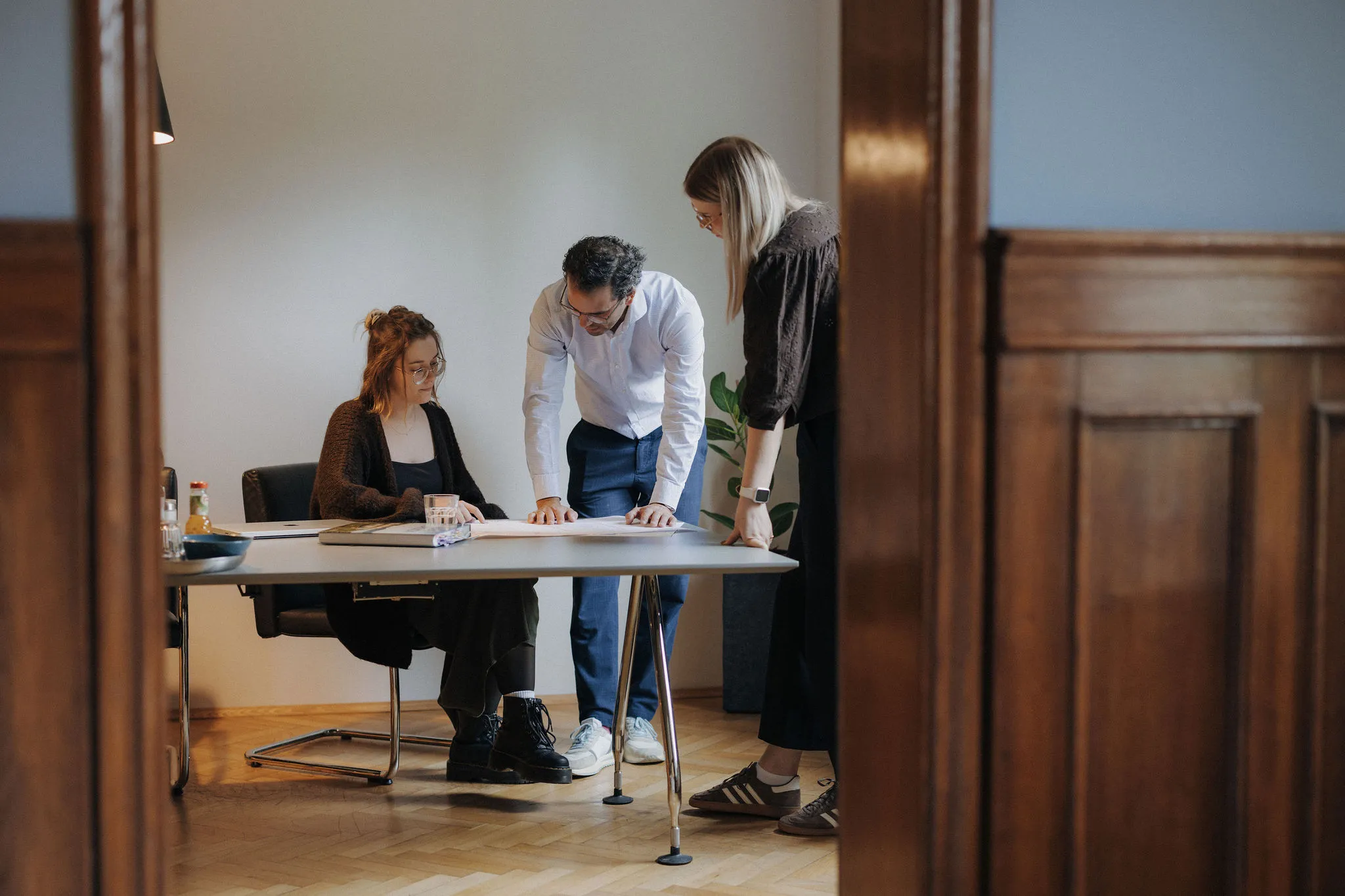 Drei Personen in einem Besprechungsraum diskutieren über Dokumente auf einem Tisch.