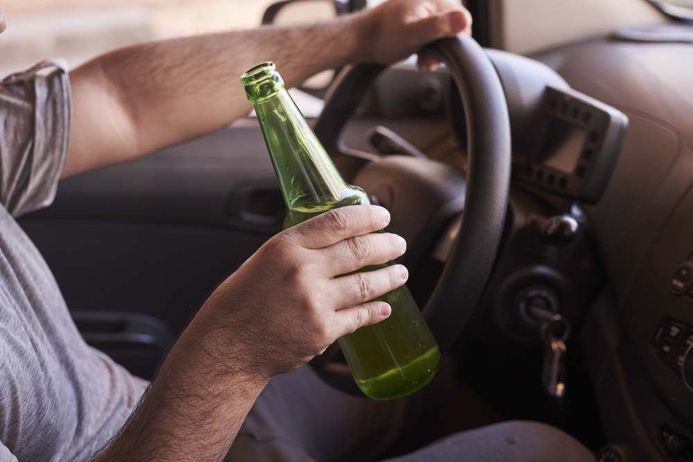 Ein Mann sitzt im Auto am Steuer mit einer Bierflasche in der Hand
