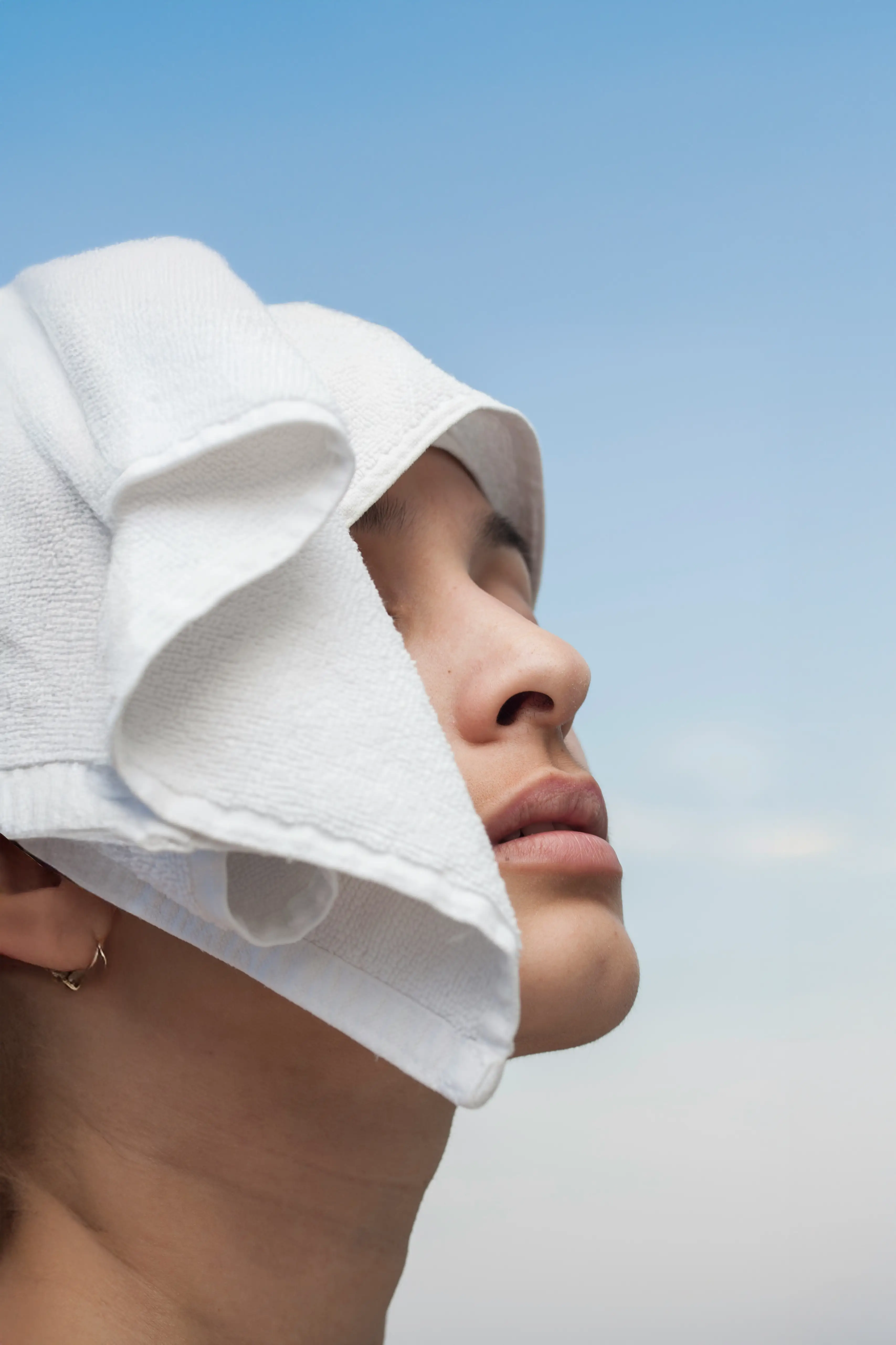 Seitliches Porträt einer Frau mit weißer Kopfbedeckung vor blauem Himmel.