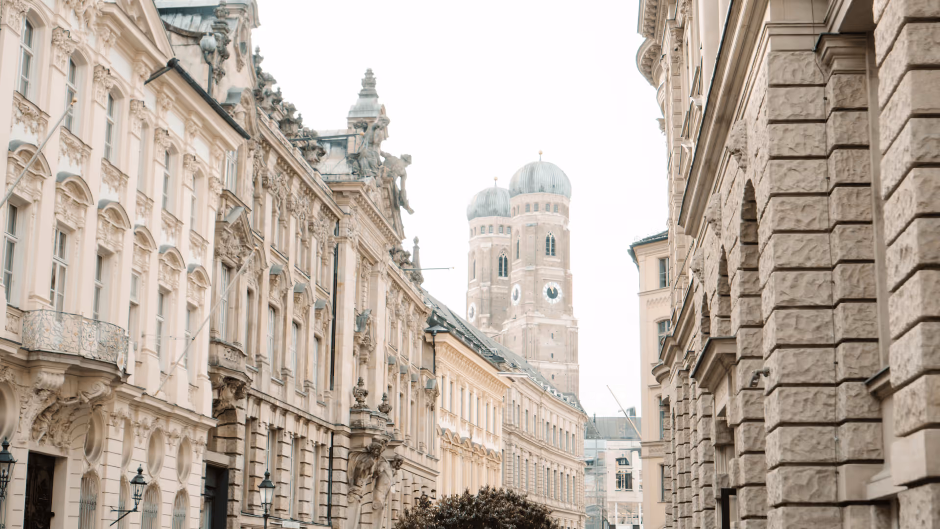 Straßenszene mit historischen Gebäuden und den Zwiebeltürmen der Frauenkirche im Hintergrund in München.