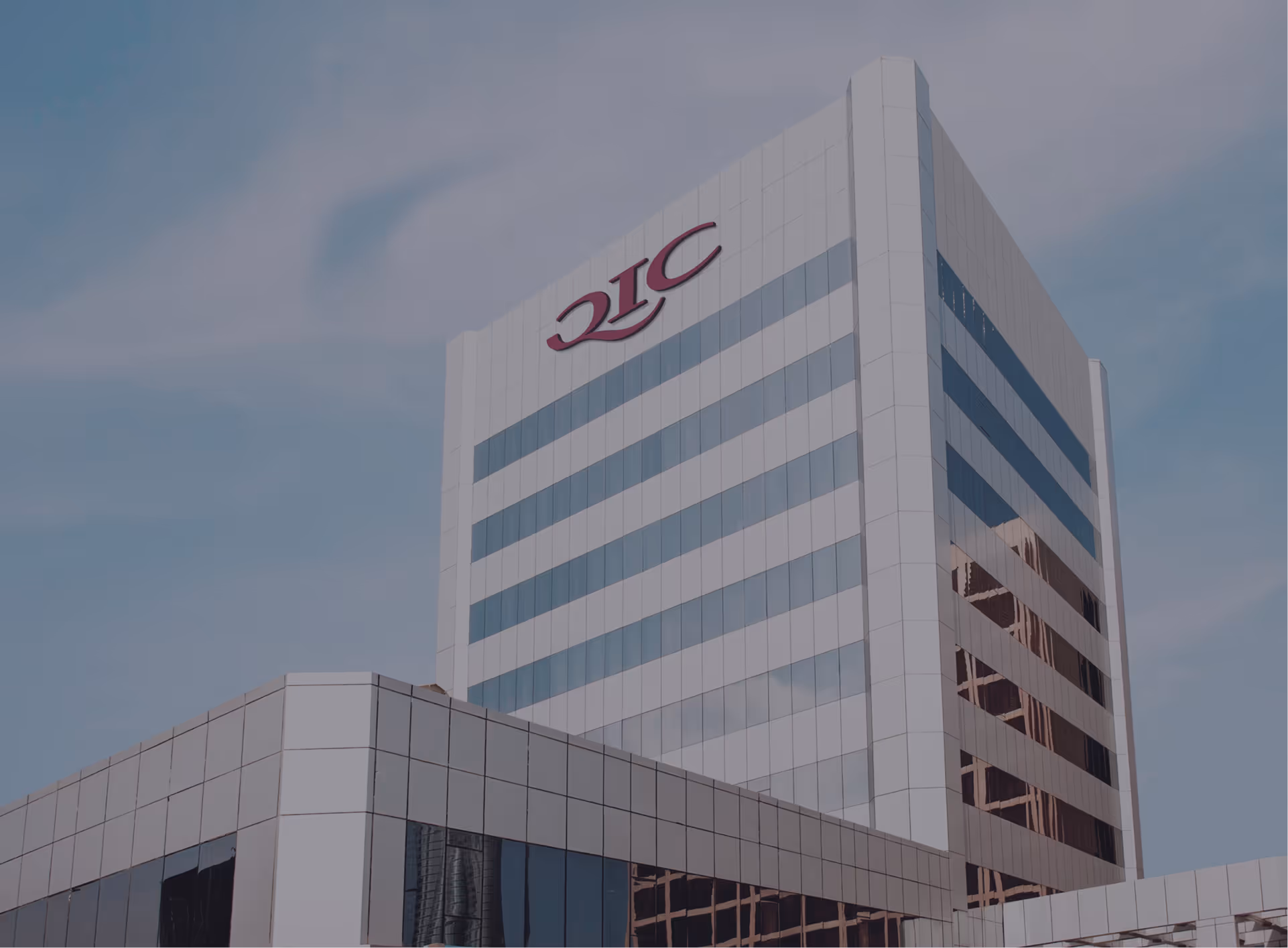 Modern white office building with reflective windows and a logo near the top against a blue sky.