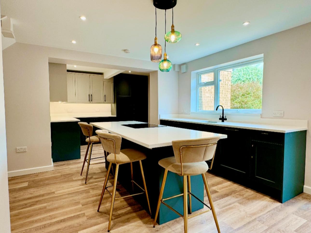 Modern kitchen with white countertops, dark cabinets, island with bar stools, and pendant lights.