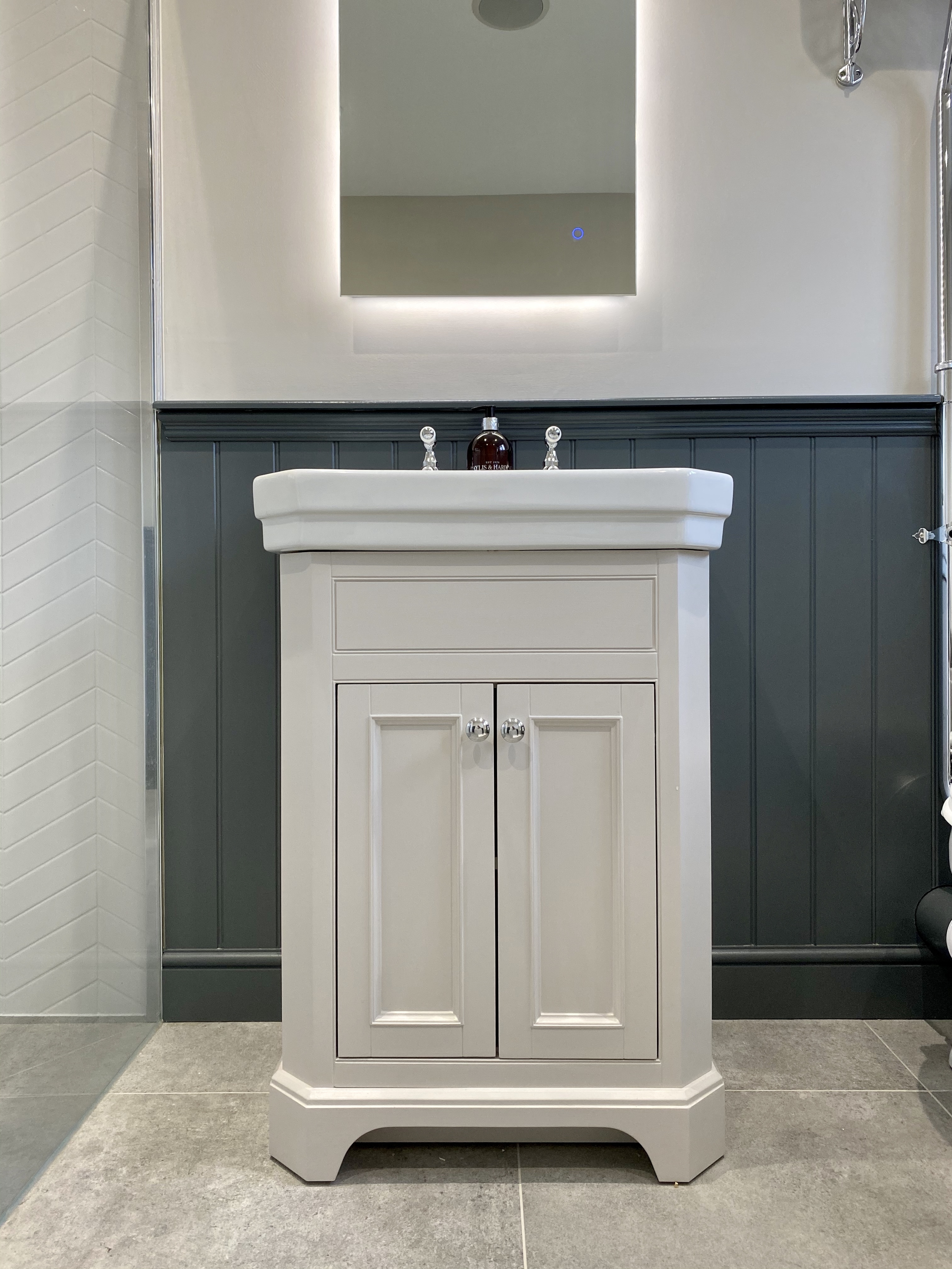 White bathroom vanity cabinet with silver knobs under a rectangular mirror and dark gray wainscoting wall.