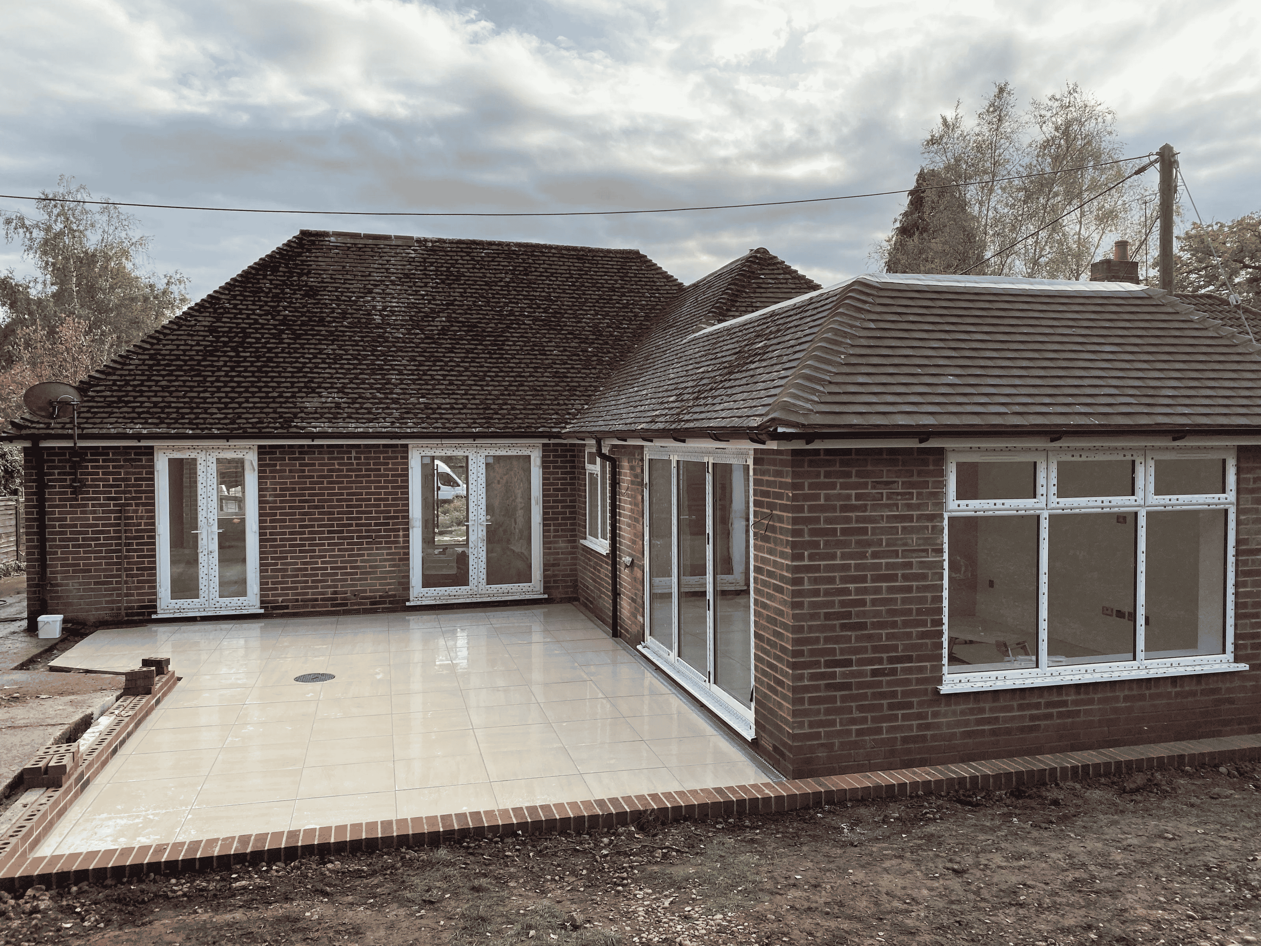 New brick house with tiled patio and multiple white-framed windows and doors under cloudy sky.