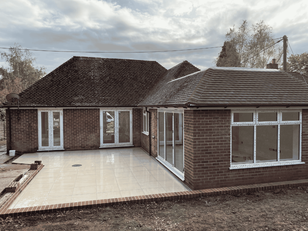Backyard view of a brick house with new tiled patio and multiple glass doors and windows.