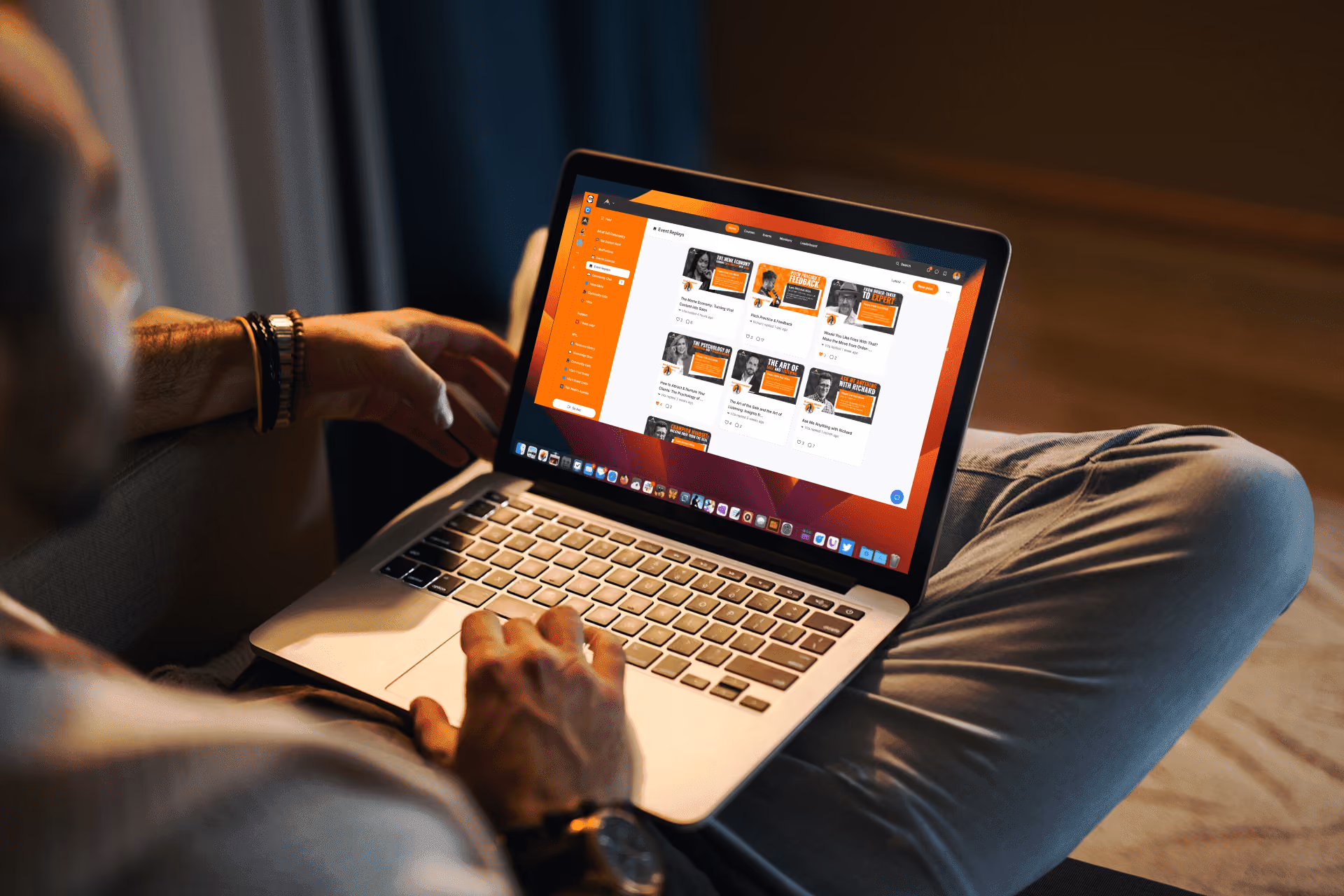 Person using a laptop showing an event replays webpage with orange and white design in a dimly lit room.