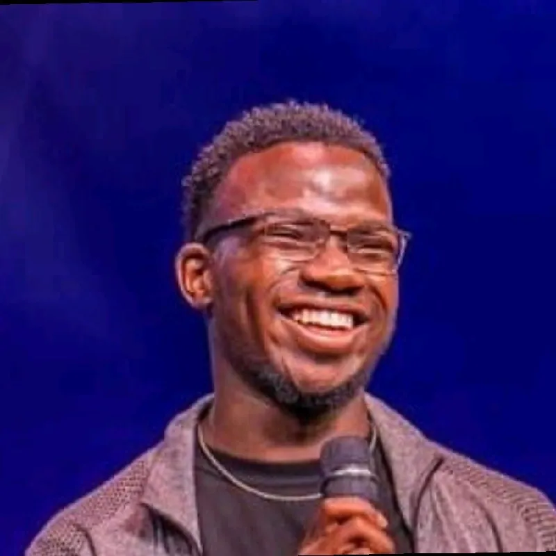 Smiling man with glasses holding a microphone against a blue background.