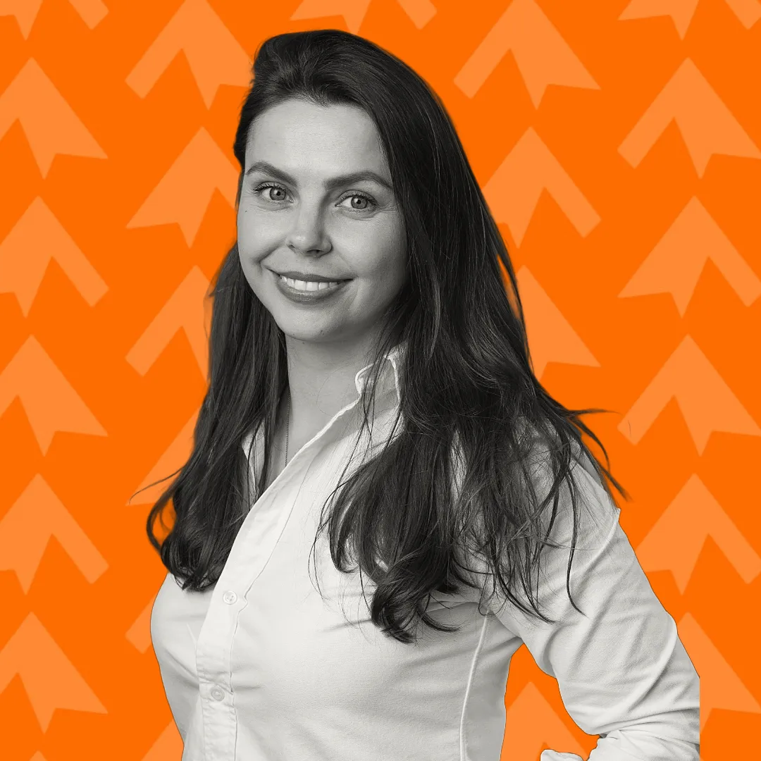 Smiling woman with long dark hair in white shirt against an orange background with arrow patterns.