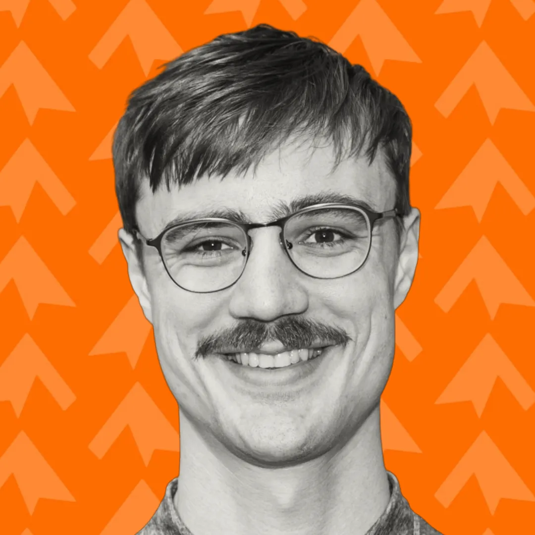 Smiling man with glasses and mustache against an orange background with arrow patterns.