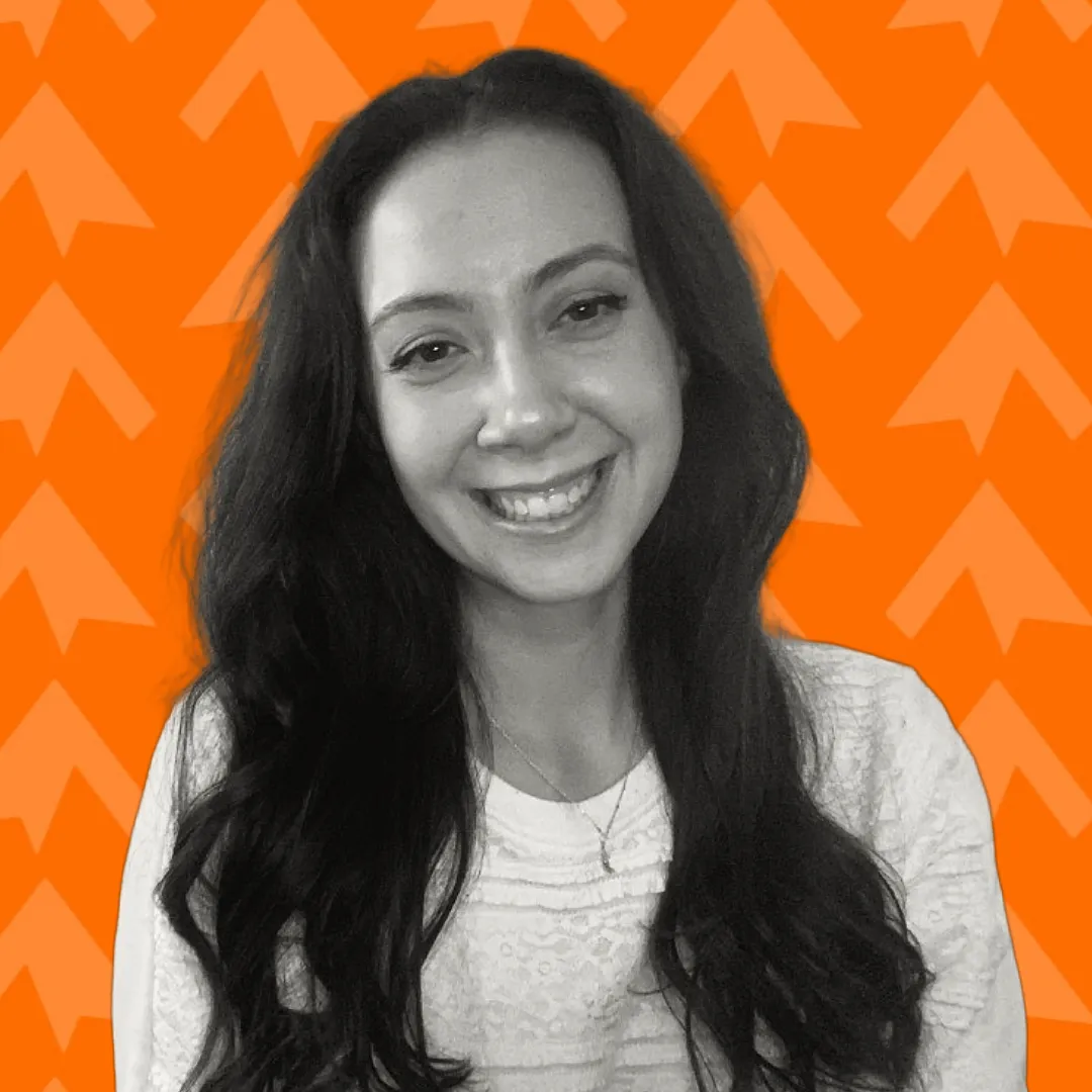 Smiling woman with long dark hair wearing a white lace top against an orange background with arrow patterns.