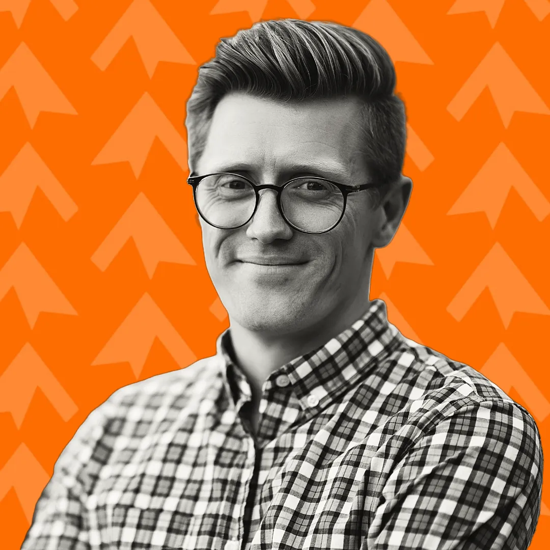 Smiling man with glasses wearing a checkered shirt against an orange background with arrow patterns.