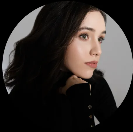 Profile of a young woman with dark hair, green eyes, and sweater, resting chin on her hand.