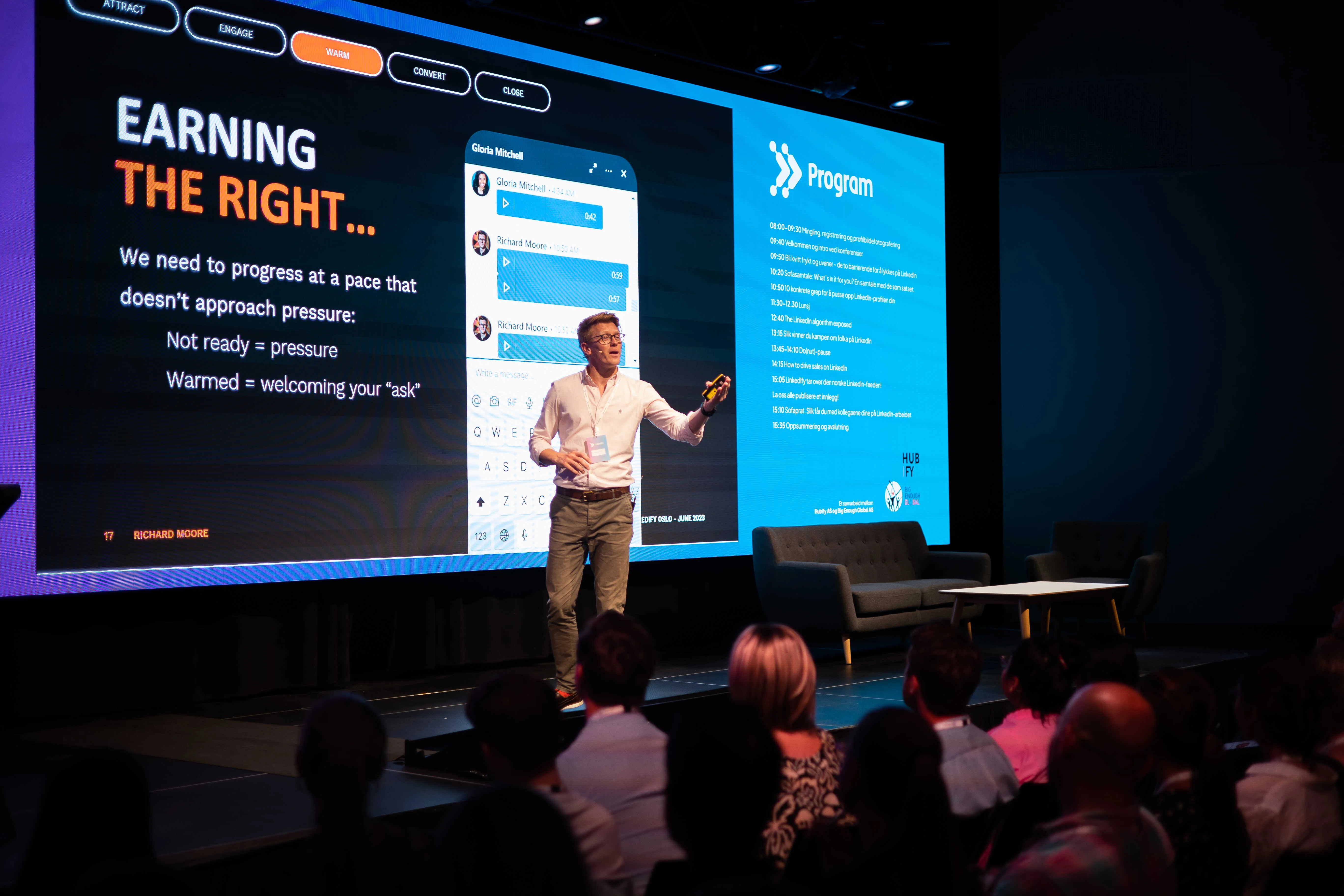 Man presenting on stage with slides about earning right and a program schedule, audience watching.