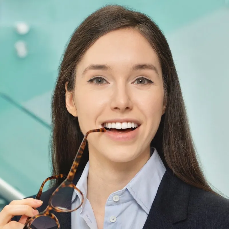 Smiling woman holding tortoiseshell eyeglasses near lips with aqua background.