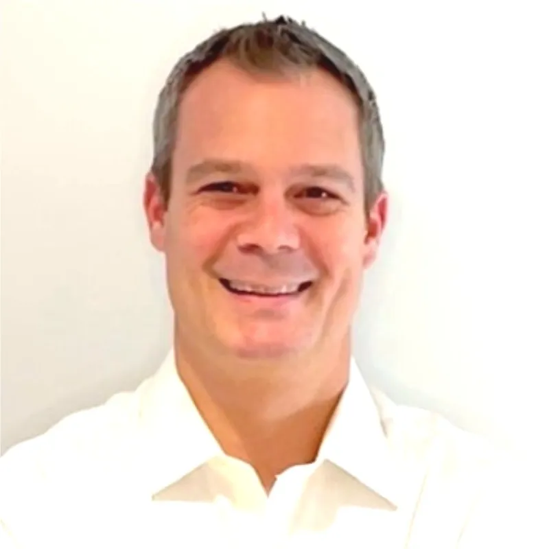 Smiling man with short hair wearing a white collared shirt against a white background.