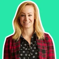 Smiling woman with blonde hair wearing a black patterned shirt and red plaid jacket on turquoise background.