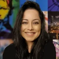 Smiling woman with long black hair and dark shirt against colorful blurred background.