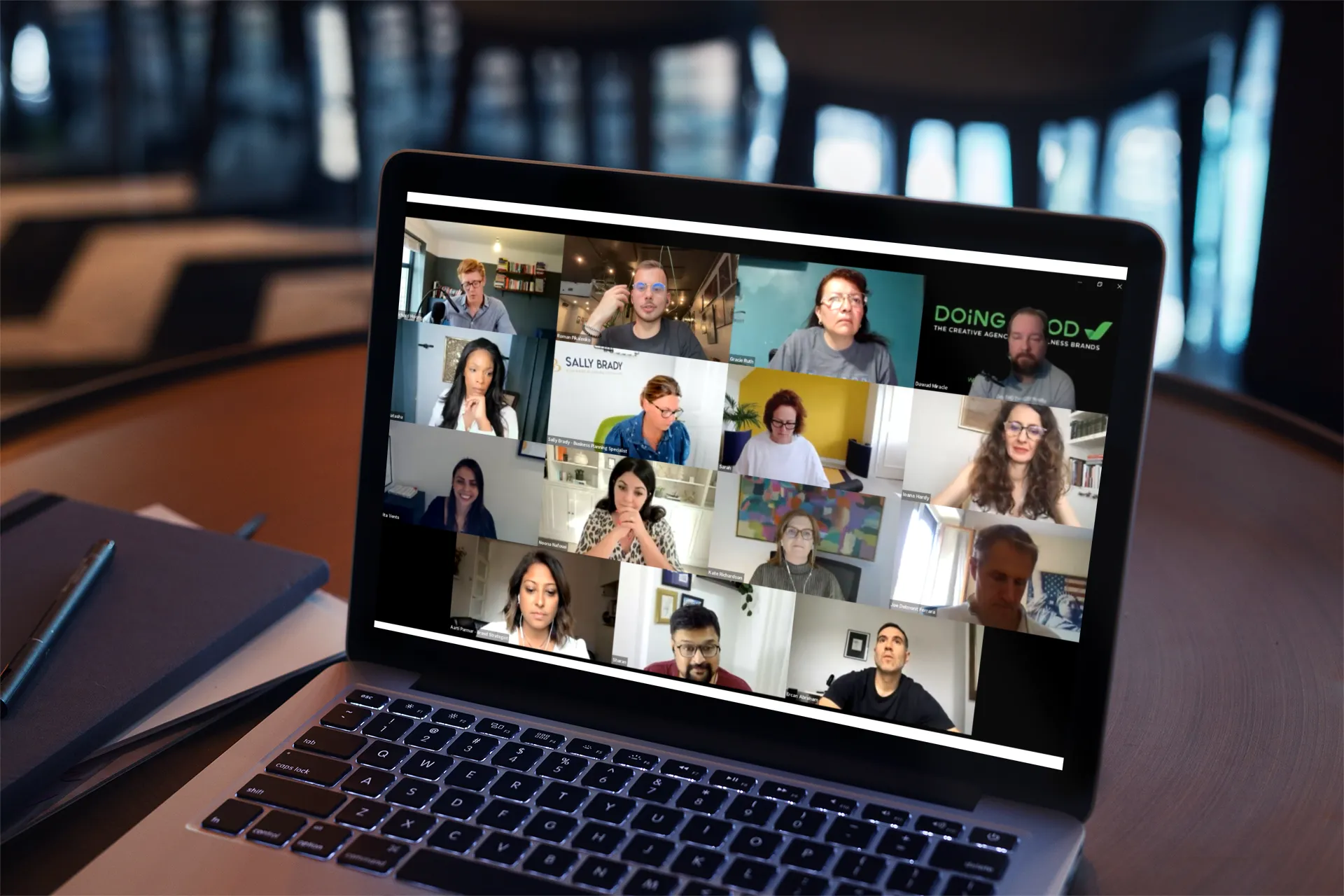 Laptop on a table showing a video conference with 16 participants in a grid layout.