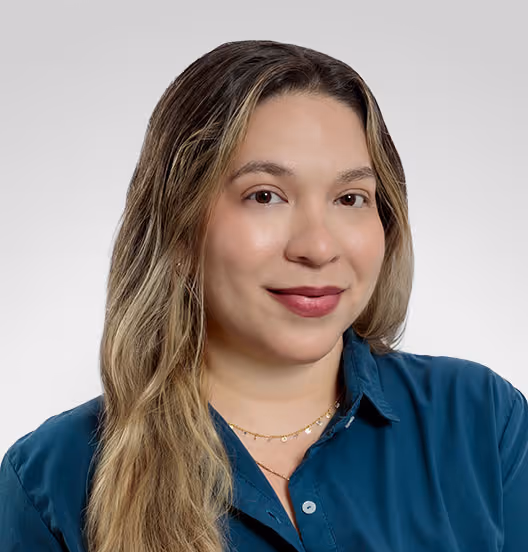 Portrait of a woman with long blonde hair wearing a teal button-up shirt and delicate gold necklaces, smiling softly against a light gray background.
