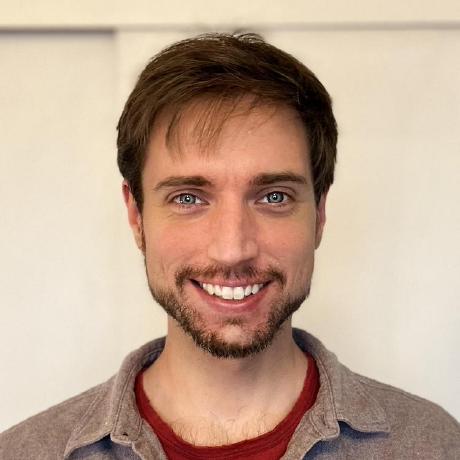 Smiling young man with short brown hair and blue eyes wearing a red shirt and beige jacket.