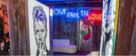 Art gallery hallway with black and white portraits on the walls and neon sign reading 'DON'T FALL IN LOVE' above a white couch.