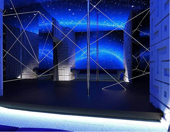 Modern room with a black stage, silver poles, geometric patterned walls, and a starry blue galaxy ceiling and back wall.