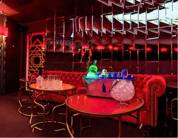 Chic lounge with red velvet tufted sofa, mirrored wall, and tables holding ice bucket with drinks and glassware.