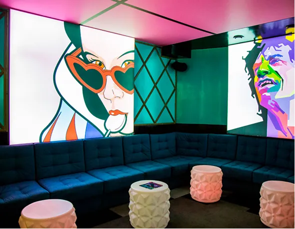 Modern lounge with dark teal sectional sofa, three white textured stools, and colorful pop art portraits on the walls.