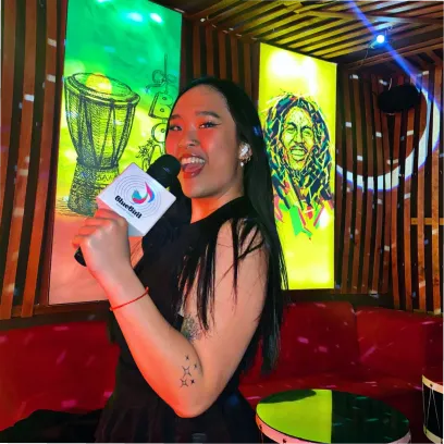 Young woman singing into a microphone in a vibrant karaoke room with colorful wall art.