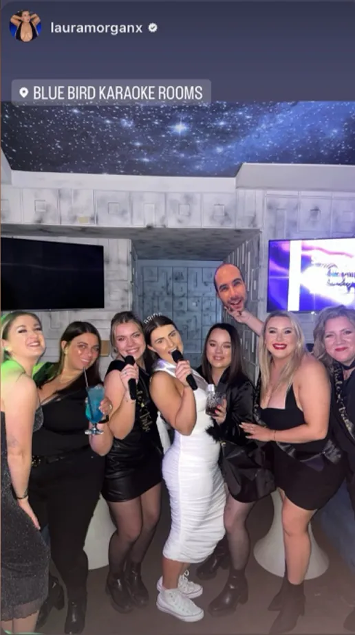 Seven people posing and singing in a karaoke room with starry ceiling decor, one person holding a head mask prop.