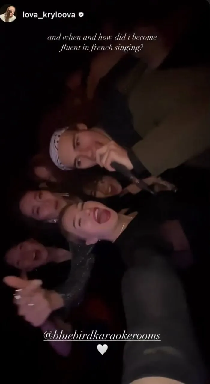 Three young adults enjoying drinks in a dimly lit room with a colorful cosmic background projection.