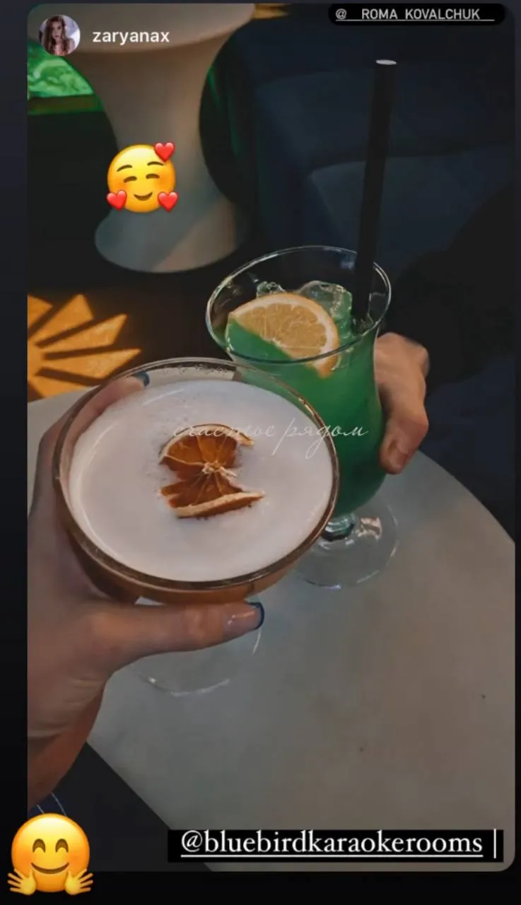 Three young adults enjoying drinks in a dimly lit room with a colorful cosmic background projection.