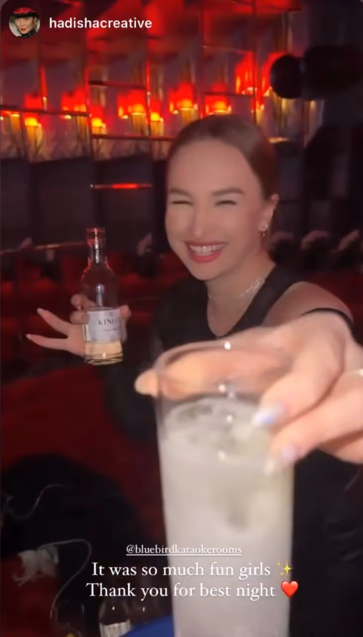 Three young adults enjoying drinks in a dimly lit room with a colorful cosmic background projection.