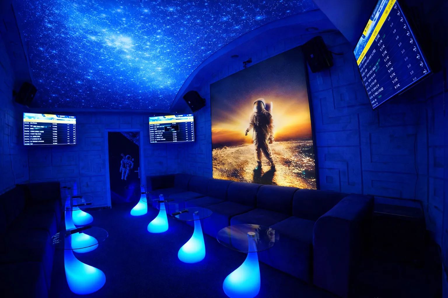 Modern room with a black stage, silver poles, geometric patterned walls, and a starry blue galaxy ceiling and back wall.