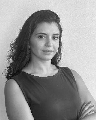 Black and white portrait of a woman with long dark hair wearing a sleeveless top and looking confidently at the camera with arms crossed.