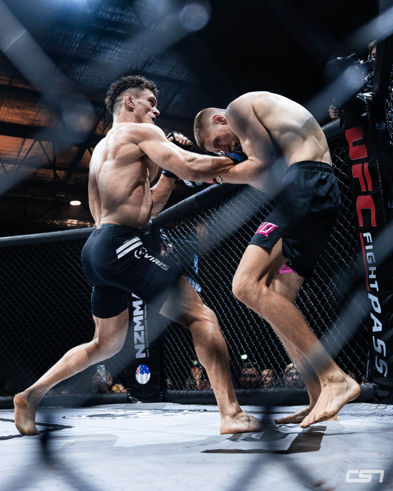 Mixed martial arts athletes clinching against the cage during a professional fight