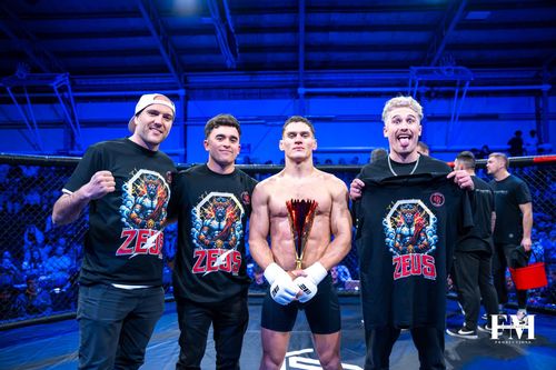 Athlete holding trophy alongside coaching team after a fight