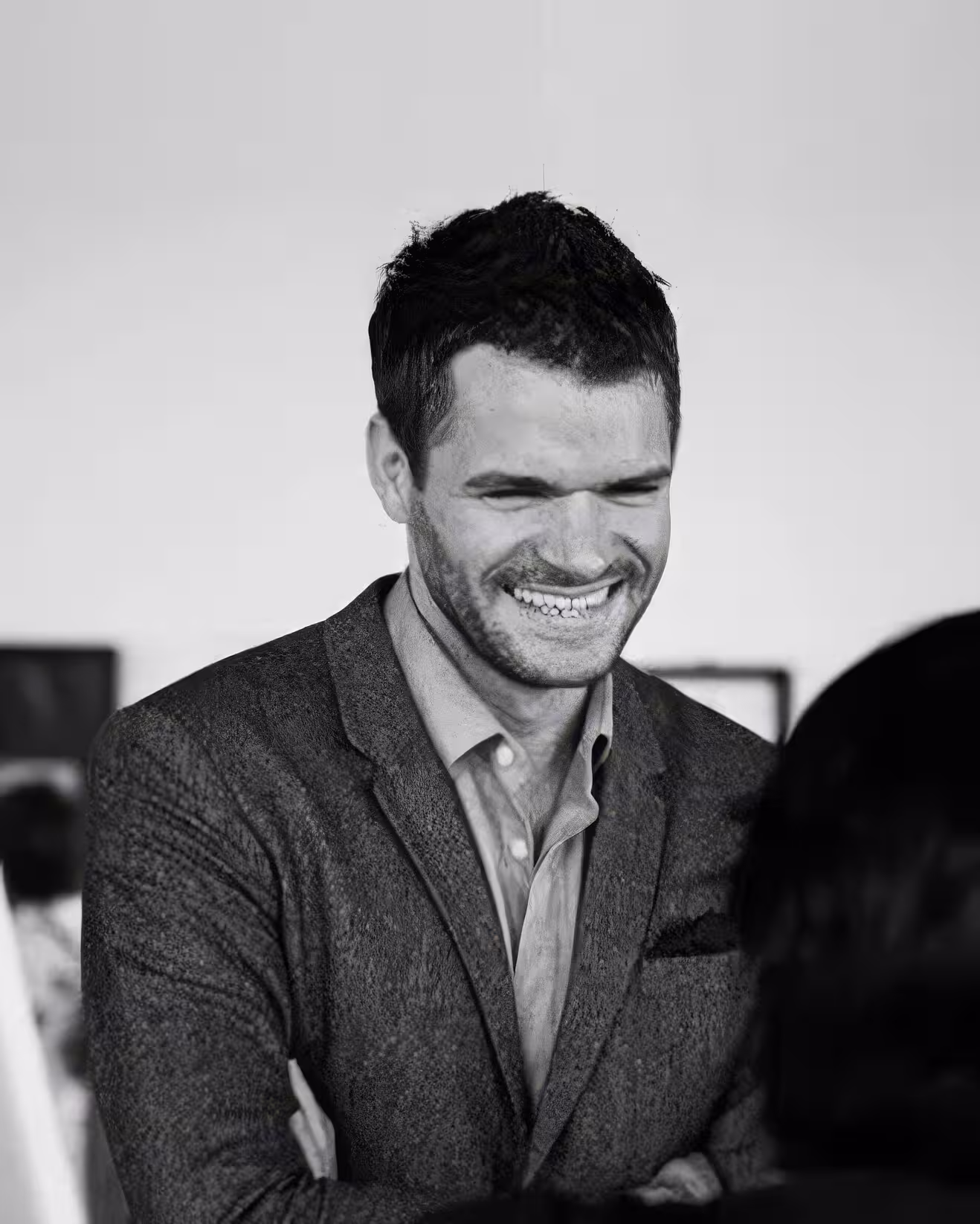 Smiling man in a suit with arms crossed looking down, black and white photo.