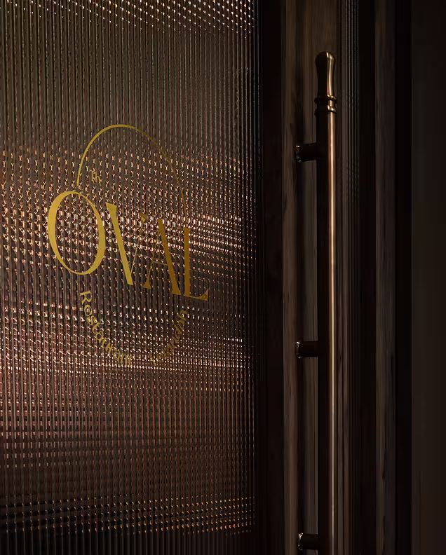 Textured glass door with the golden logo and text 'OVAL Restaurant & Bar' and a metallic handle on the right side.