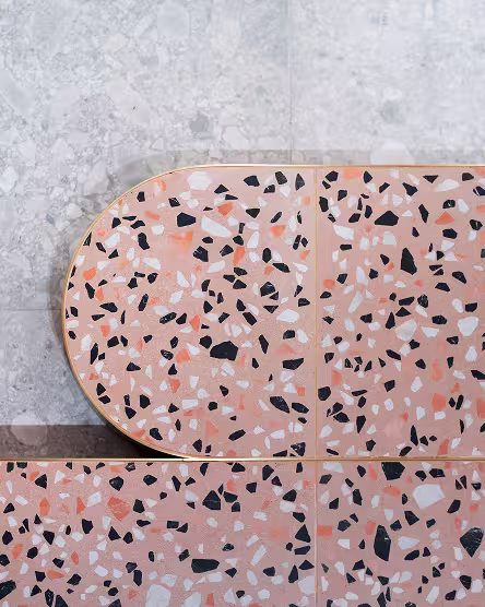 Close-up of pink terrazzo tiles with white, black, and coral chips arranged on a light gray stone surface.