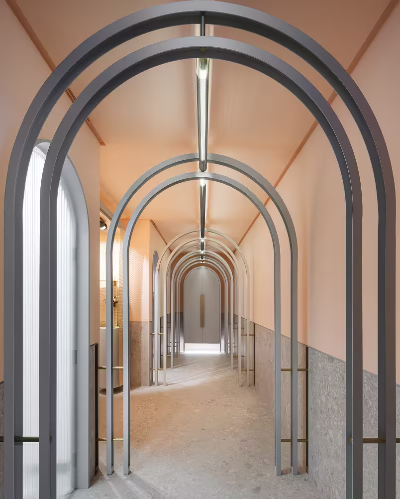 Minimalist corridor with multiple gray metal arch frames and soft peach walls leading to a closed door.
