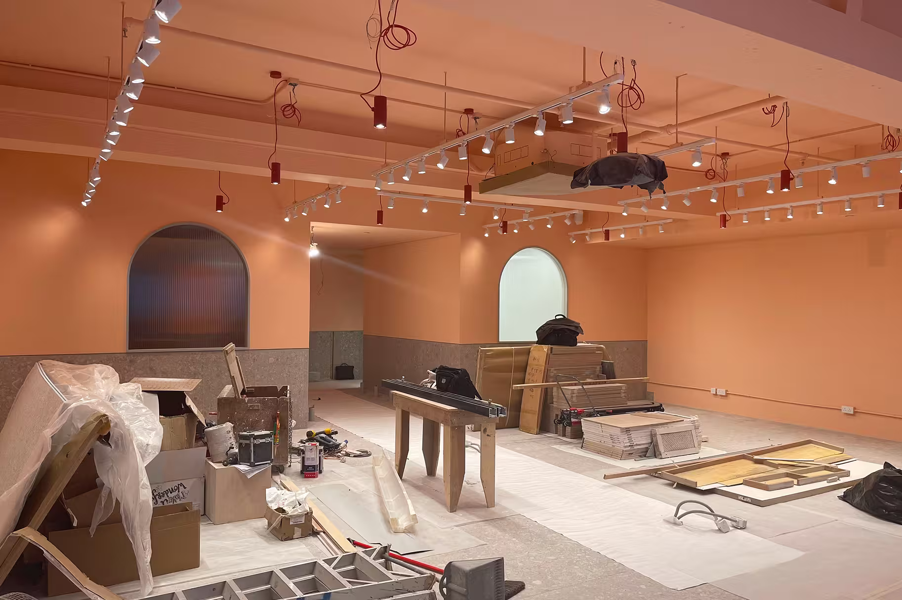 Interior space under renovation with peach walls, arched windows, multiple construction materials, and ceiling-mounted lights.