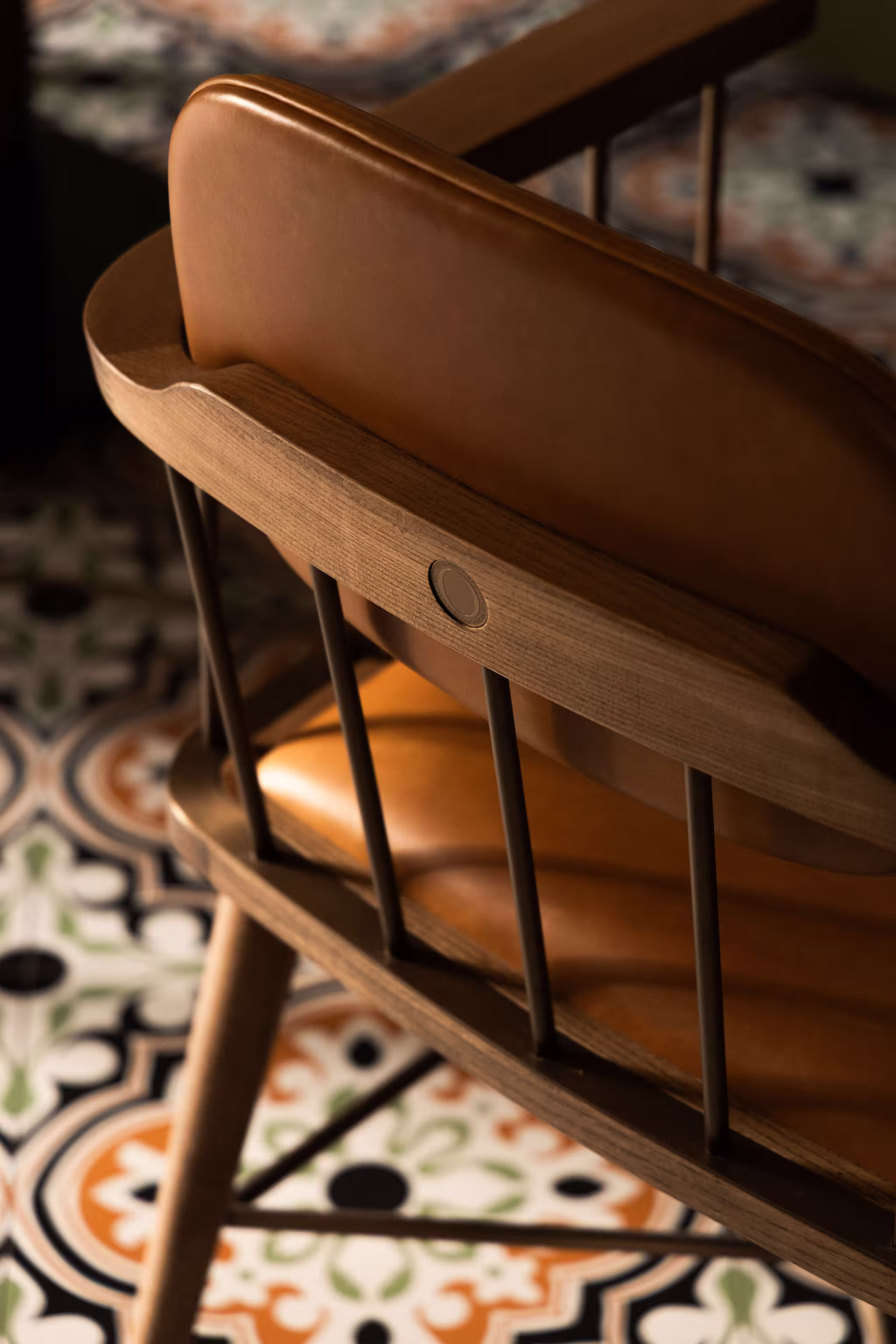 Close-up of a wooden chair with a brown leather backrest and seat on colorful tile flooring.