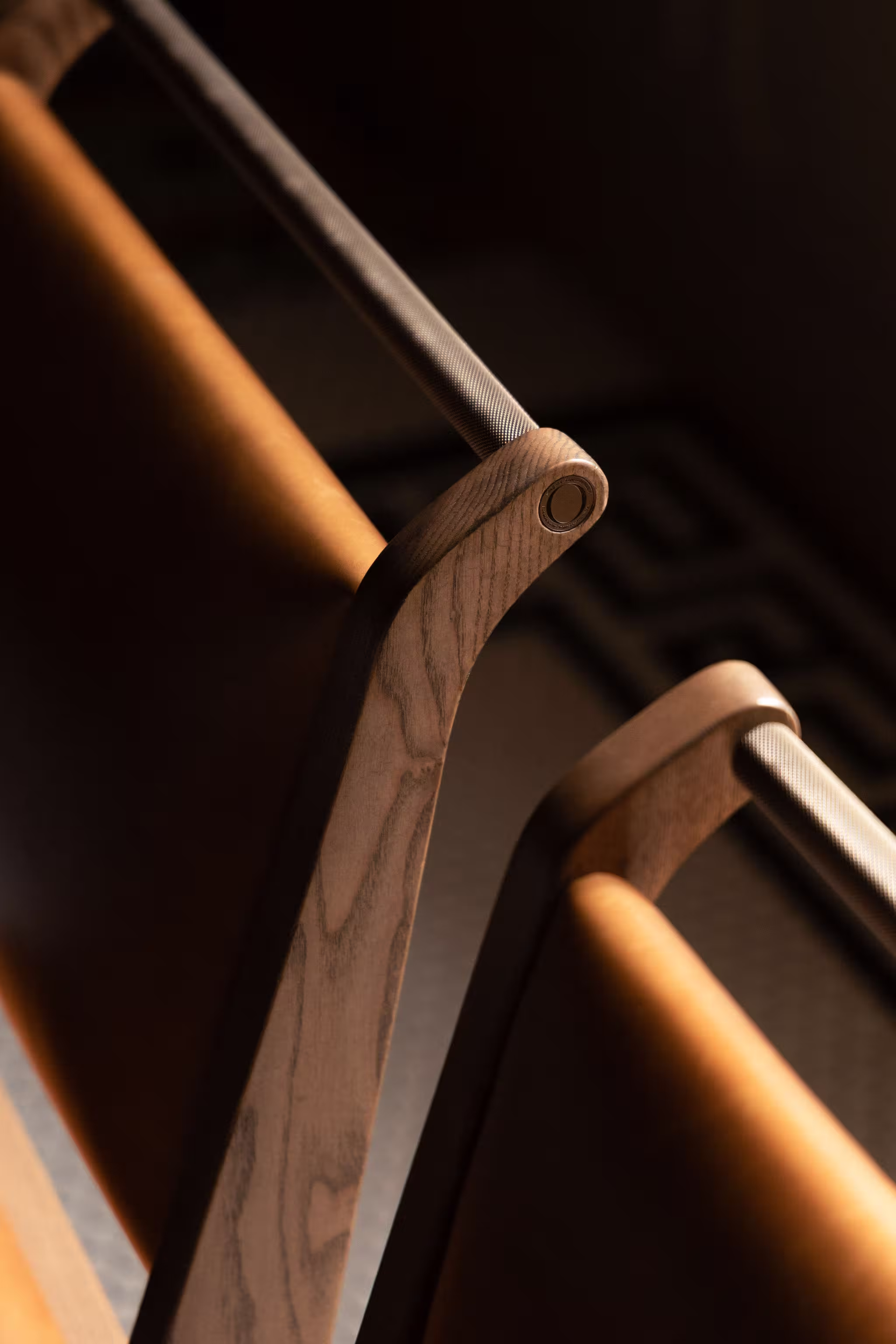 Close-up of wooden chair backs with textured metal bars in warm lighting.